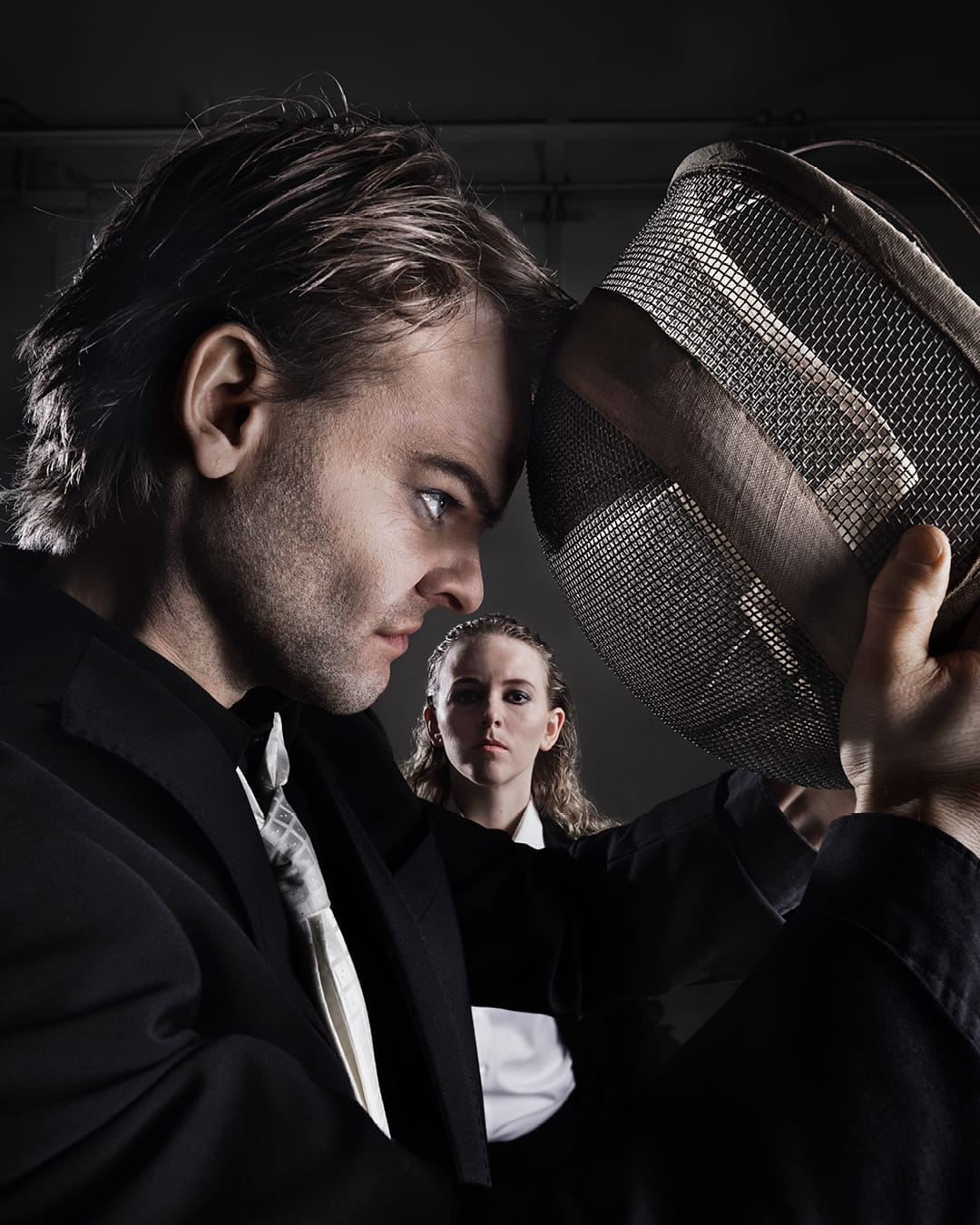 Hamlet lutar sitt huvud mot en fäktningsmask. En kvinna syns i bakgrunden.