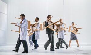 Skådespelarna i läkarrockar bär på stolar