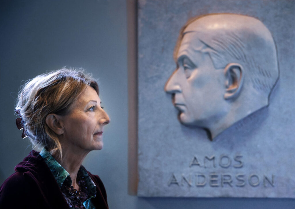 Pjäsförfattaren Gunilla Hemming står framför en relief med Amos Andersson.